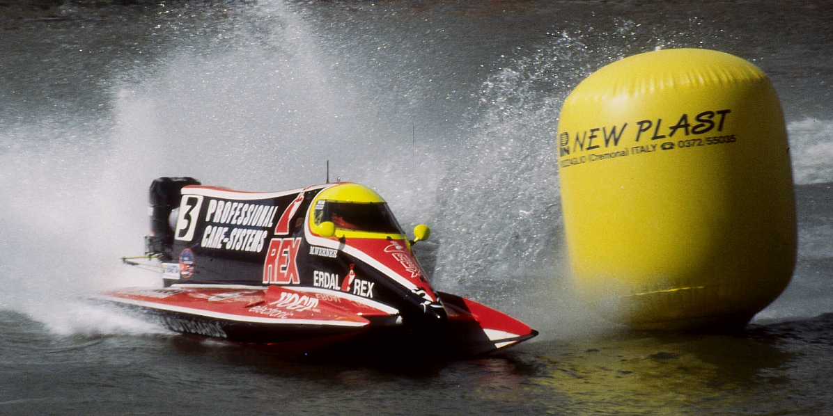 A red Formula 1 powerboat rounds a yellow buoy, throwing up a plume of spray.